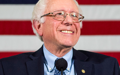 Bernie Sanders speaking at an event with the American flag in the background