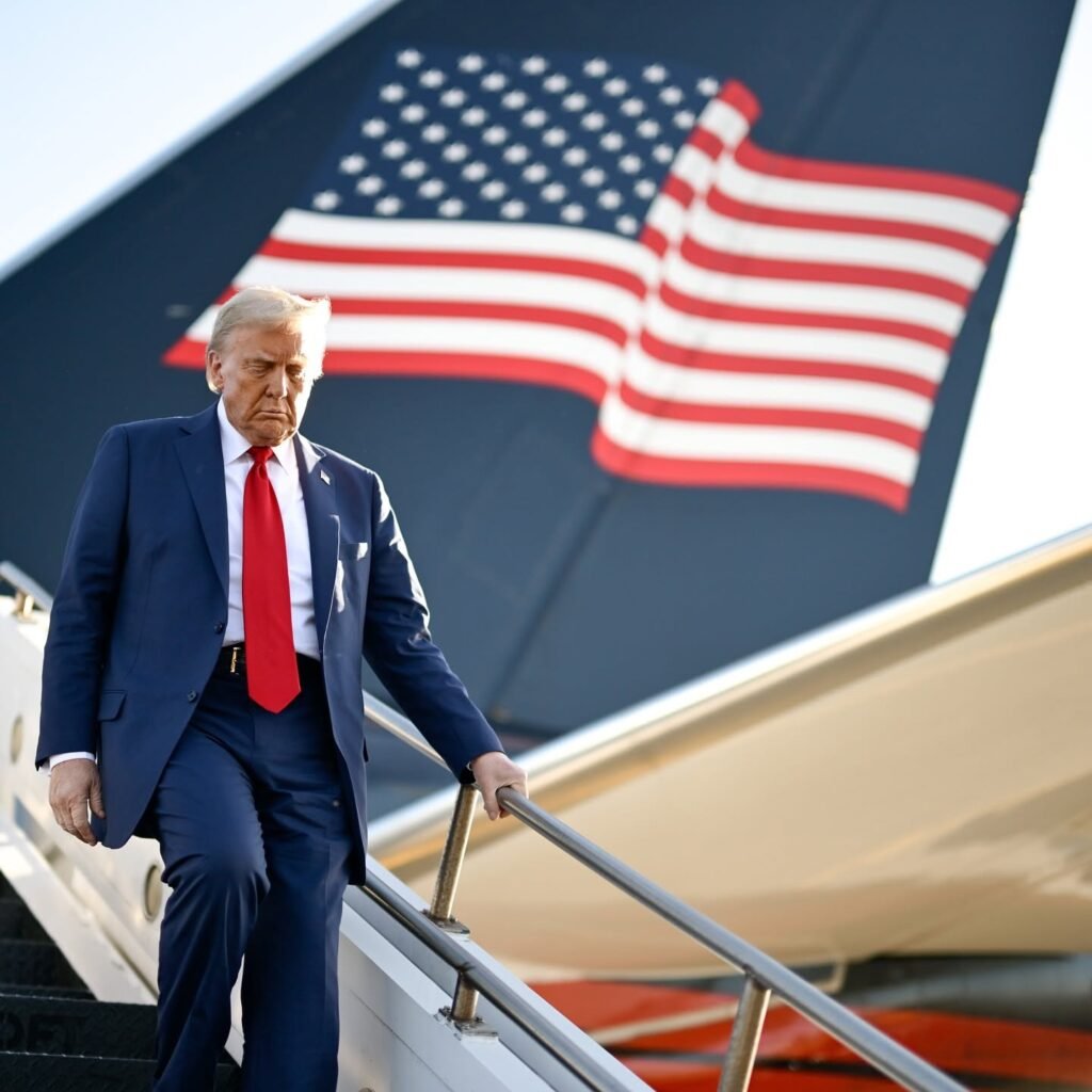 U.S. president walking down the stairs of an aircraft with an American flag in the background