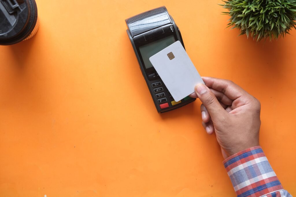 Hand holding a credit card over a point-of-sale payment terminal.
